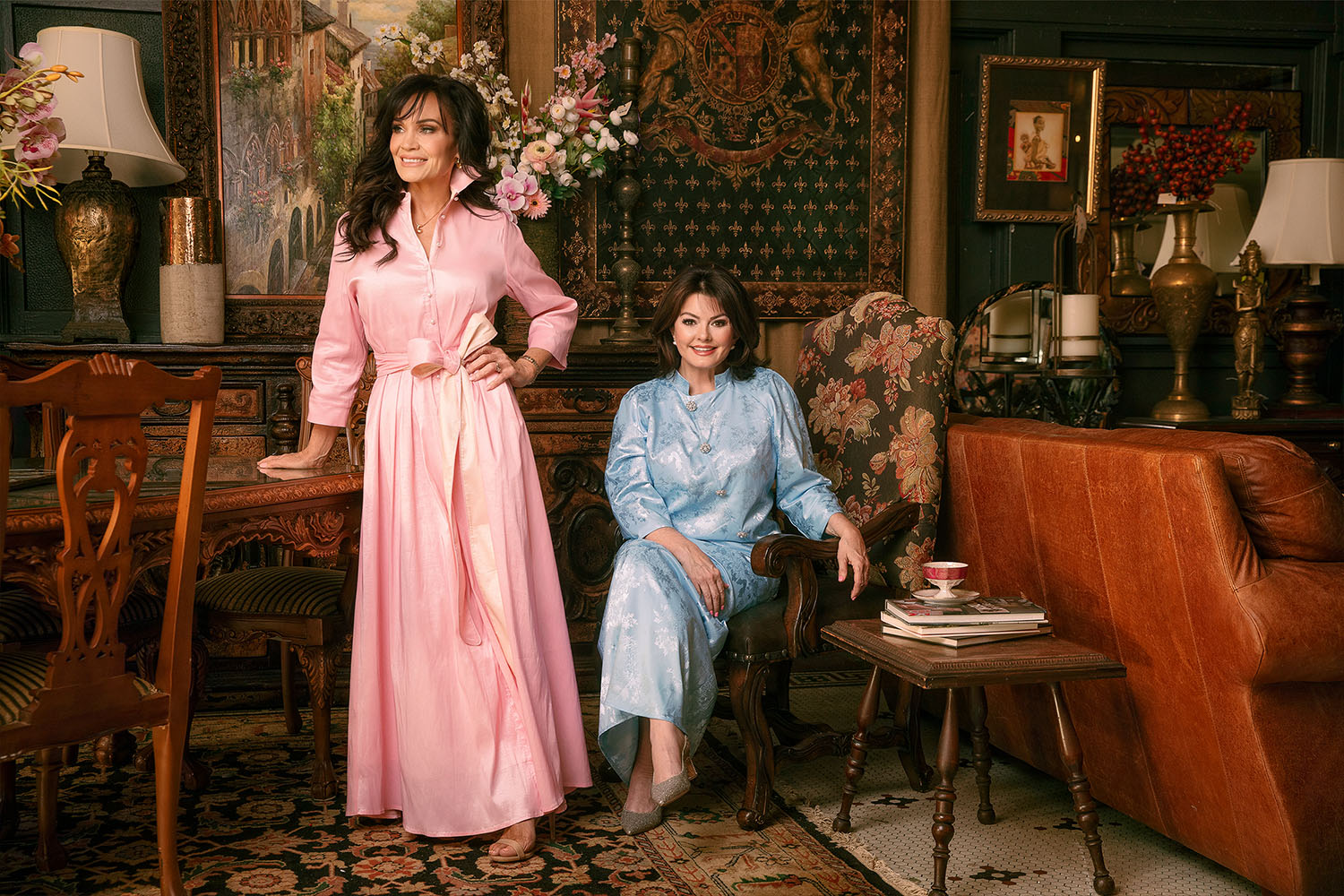 Two women in formal attire standing in a decorated room with furniture and decor.